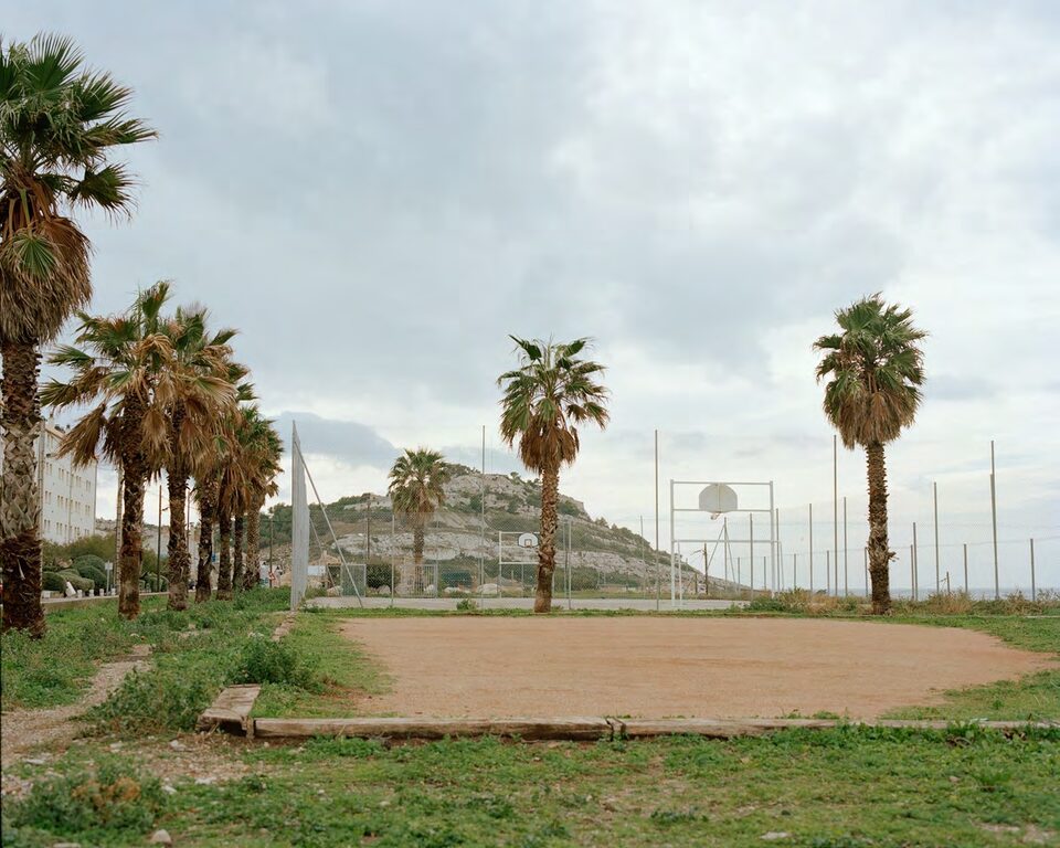 Empty basketball court with palm trees, fencing and an overcast sky
